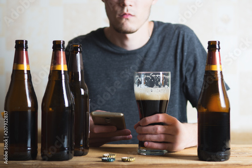 A man drinks a beer and calls on the phone