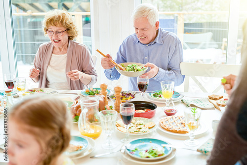 Portrait of happy family enjoying dinner together sitting round festive table with delicious dishes, focus two grandparents, copy space