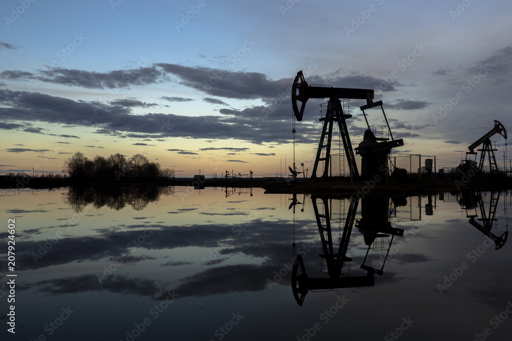 Naklejka premium The beam pumping unit is homework, sunset in oil field. Oil pump oil rig energy industrial machine for petroleum. The pumping unit as the pump installed on a well. Equipment of oil fields.