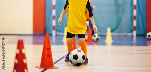 Football futsal training for children. Soccer training dribbling cone drill. Indoor soccer young player with a soccer ball in a sports hall. Player in orange uniform. Sport background
