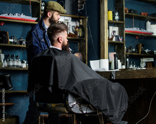 Hipster client got new haircut. Barber with bearded man looking at mirror, barbershop background. Haircut concept. Barber finished trimming. Client and professional master checking result © be free