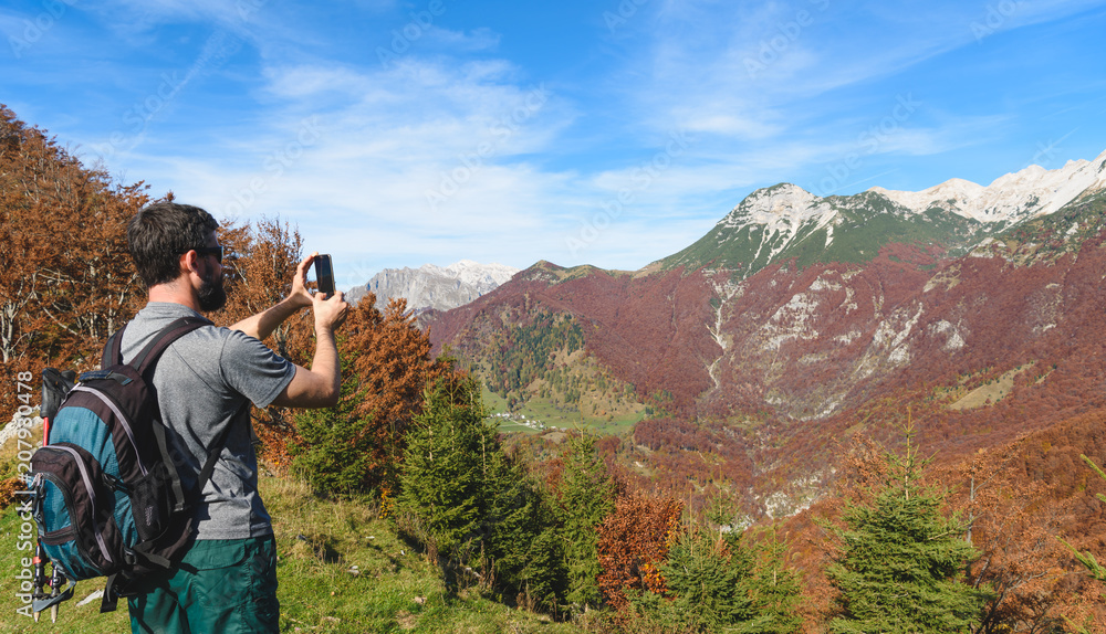 Hiking in Alps mountains. Man Traveler with Backpack hiking in the Mountains and making photo with his smartphone. mountaineering sport lifestyle concept