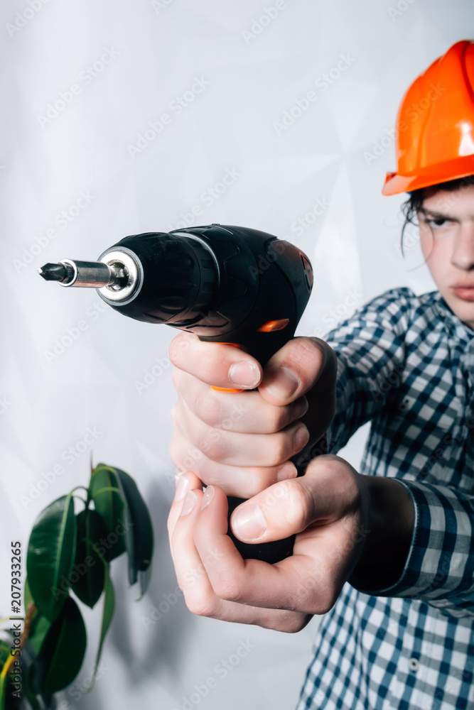 attractive and confident constructor carpenter or builder man working wood with electric drill at industrial construction site.The builder or the repairman holds in his hand a drill attractive and confident constructor carpenter or builder man working wood with electric drill at industrial construction site.The builder or the repairman holds in his hand a drill