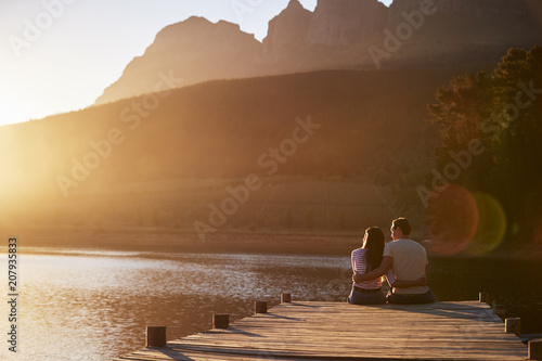 Romantic Couple Sitting On Wooden Jetty By Lake