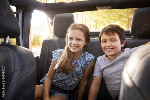 Children Sitting In Back Seat Of Open Top Car On Road Trip