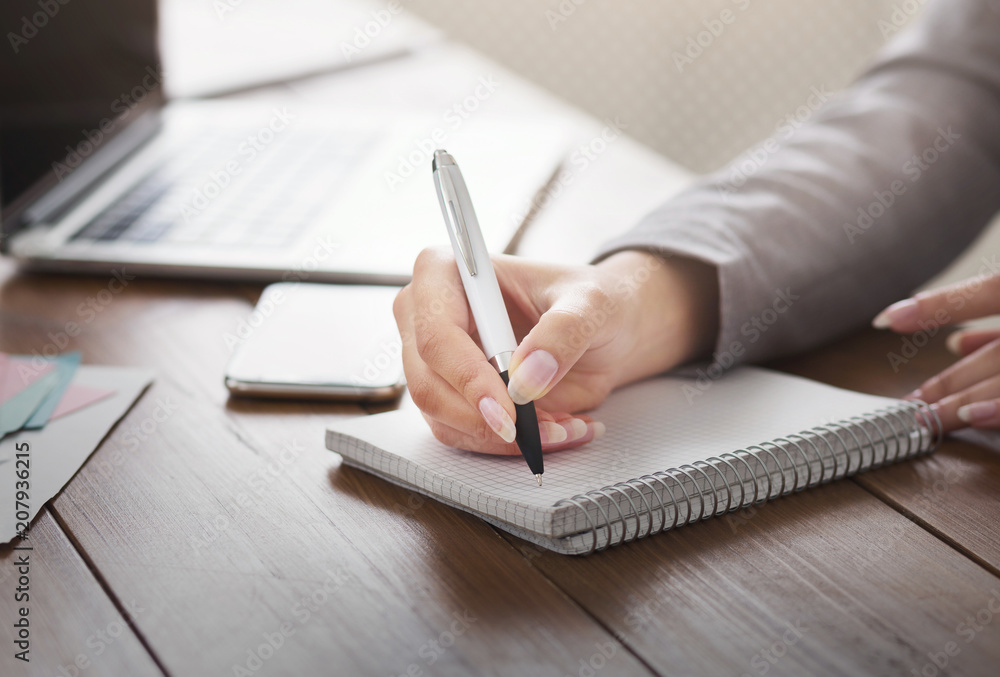 Female hand taking notes at office table Female hand taking notes at office table