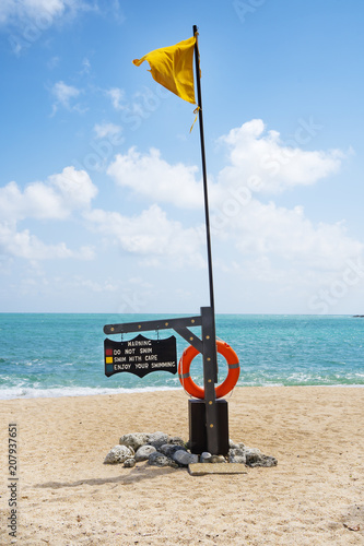 Safe swiming warning sign and yellow flag on a tropical beach