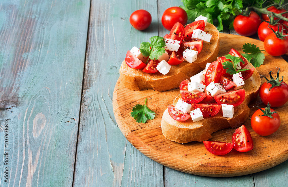 Italian bruschetta with tomato and cheese on toasted toast, blue wooden background. Copy space, selective focus.