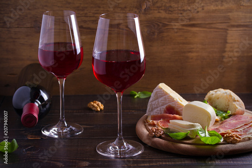 Glasses of wine with cheese, bread, nuts, prosciutto and basil. Wine and food on wooden table. horizontal, room for text