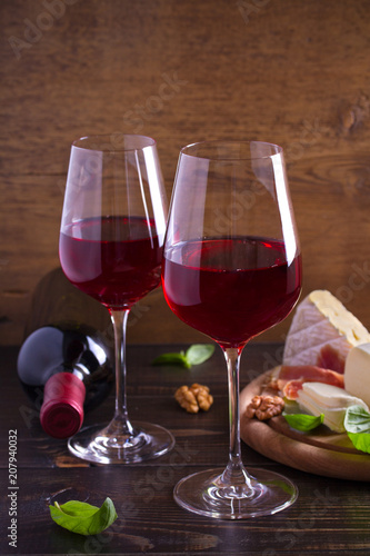 Glasses of wine with cheese, bread, nuts, prosciutto and basil. Wine and food on wooden table. vertical, room for text