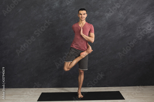 Young flexible man practicing yoga at gym