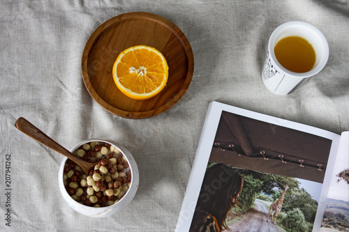 A delicious vitamin nutritious breakfast from freshly squeezed orange juice in a glass, half of an orange on a wooden round plate, cereal breakfast with milk in a clay bowl on a linen tablecloth.