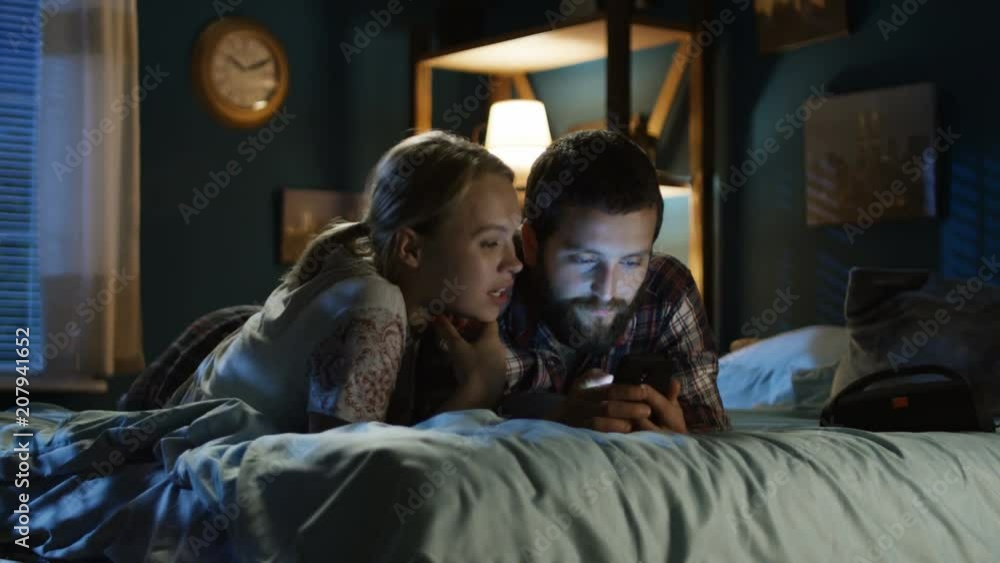 Young girl with smartphone and lying on bed in night and surfing Internet together having fun and relaxing Young girl with smartphone and lying on bed in night and surfing Internet together having fun and relaxing