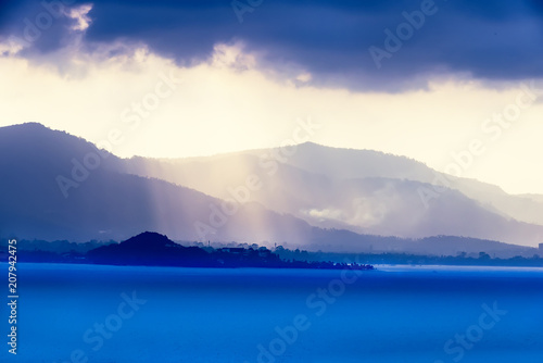 Sun rays passing through heavy storm clouds over the sea bay town. Wallpaper image.