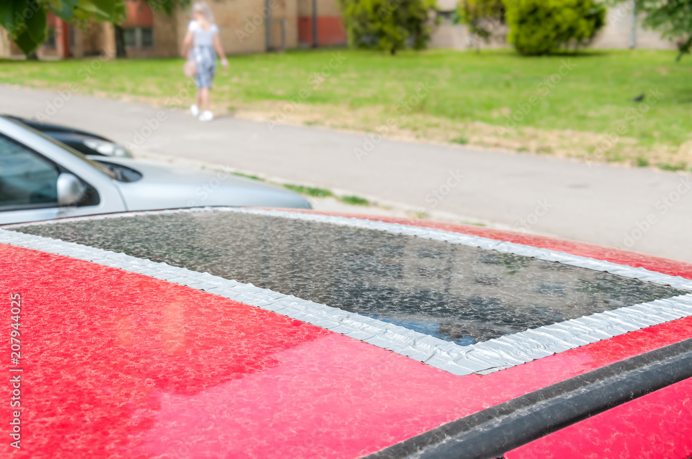 Damaged glass roof window or sunroof on the red car glued with duct
