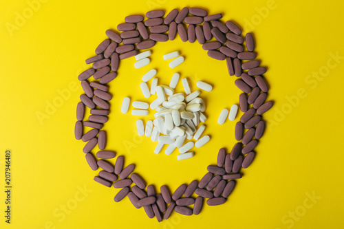 Fototapeta Naklejka Na Ścianę i Meble -  a lot of violet, oval tablets, pills scattered, scattered on a yellow background in the form of a circle, in the middle of the circle are scattered white pills, oval, space for text