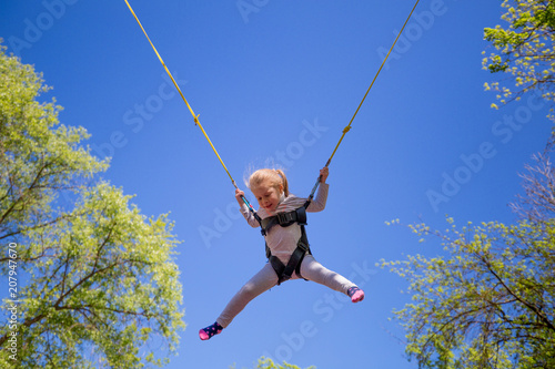 Children summer entertainment. Little girl jumping on children trampoline on blue sky backdrop.