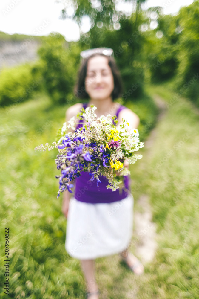 The girl is holding out a bouquet of wildflowers. The girl is holding out a bouquet of wildflowers.