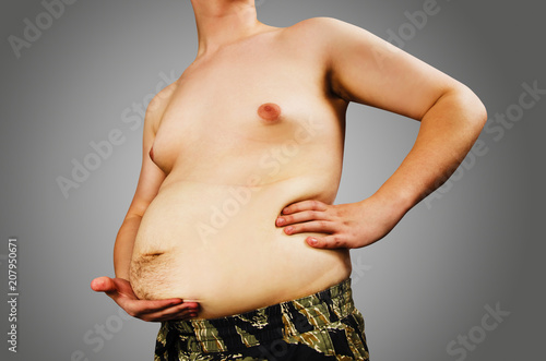 Fotografie Torso of young fat man holding his belly on gray background