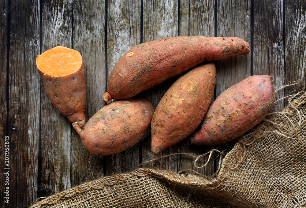 sweet potatoes over wooden background with rustic sack sweet potatoes over wooden background with rustic sack