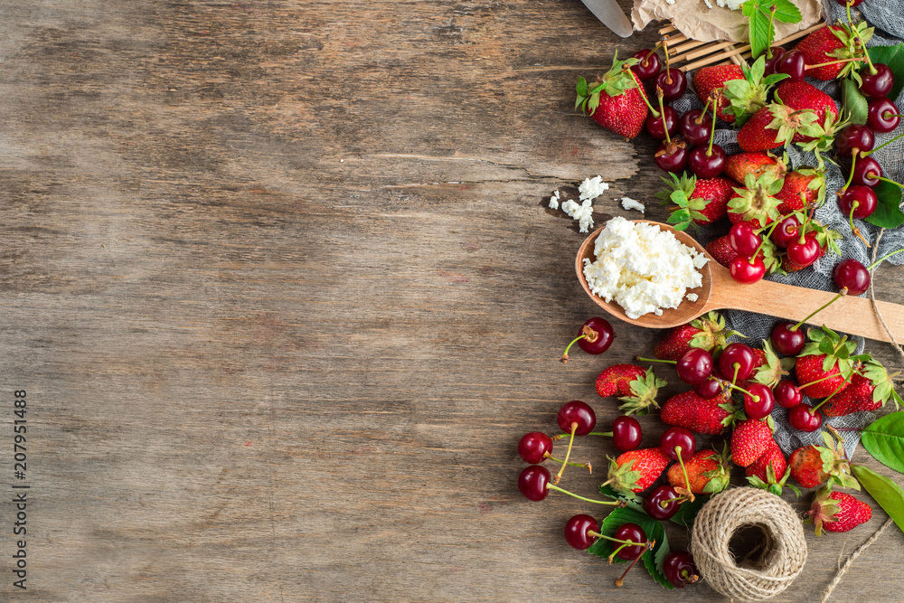 Fresh sweet cherries and strawberries with cottage cheese on wooden background. Top view. Copy space. Flatlay