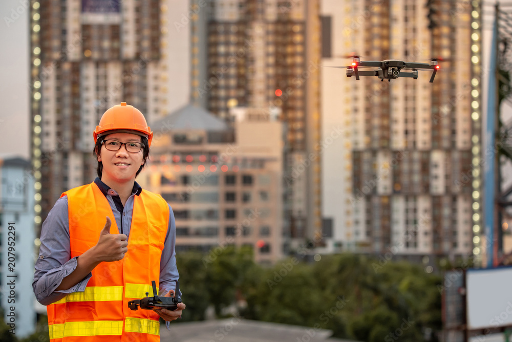 Young Asian engineer flying drone over construction site. Using unmanned aerial vehicle (UAV) for land and building site survey in civil engineering project. Young Asian engineer flying drone over construction site. Using unmanned aerial vehicle (UAV) for land and building site survey in civil engineering project.