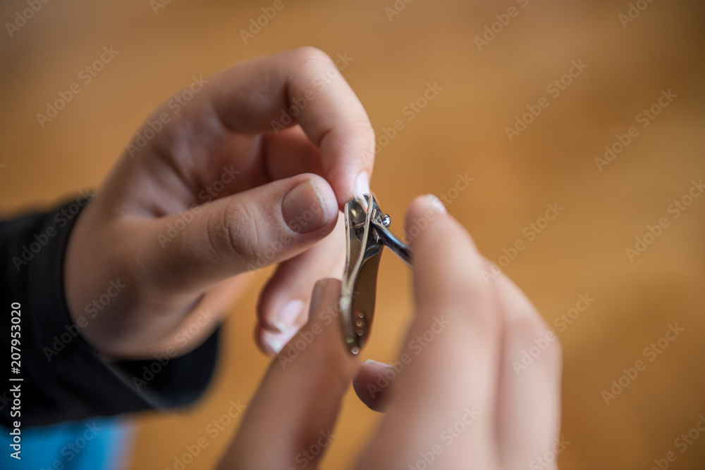 Fototapeta premium Hands of the child with nail clipper, clipping the nails on his own