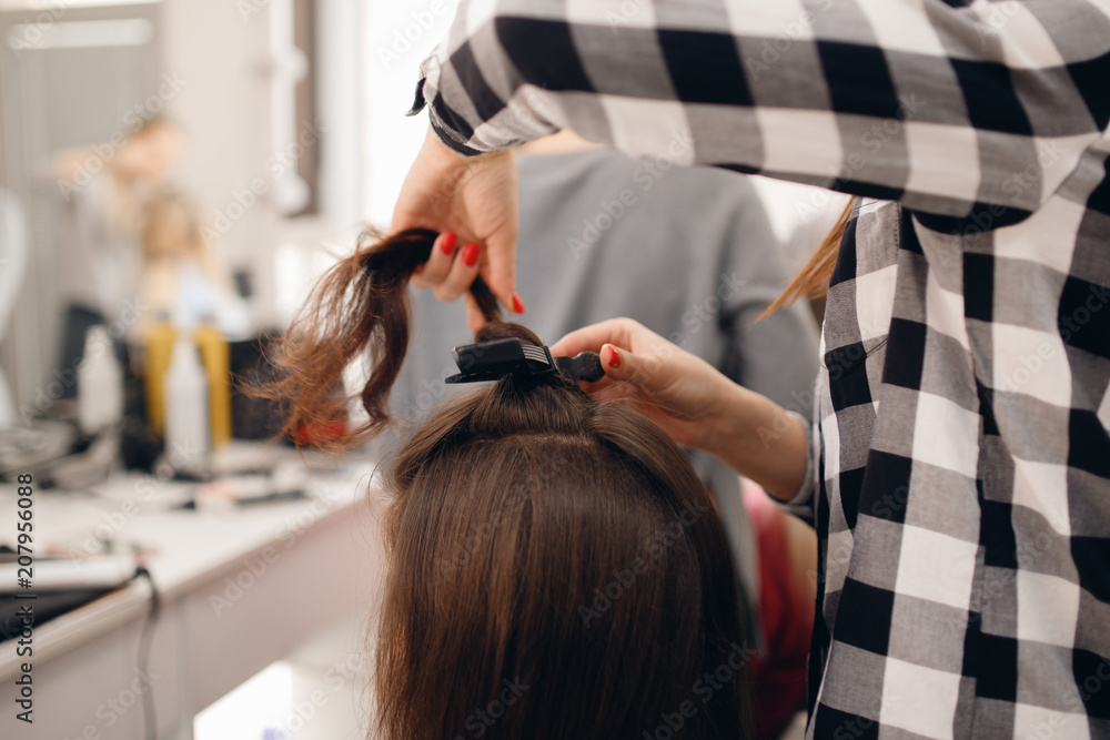 Naklejka premium Hairdresser woman straightens her hair and makes styling, close-up of curling iron in salon