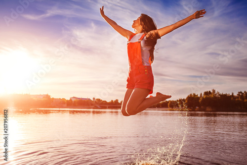 Happy and free young woman jumping and raising arms on river bank. Freedom. Active lifestyle photo