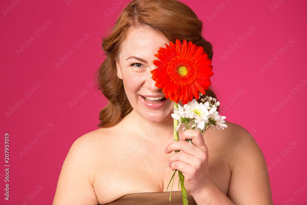 Close up female portrait. Beautiful adult woman with gerbera flowers on a pink background. Red hair woman.