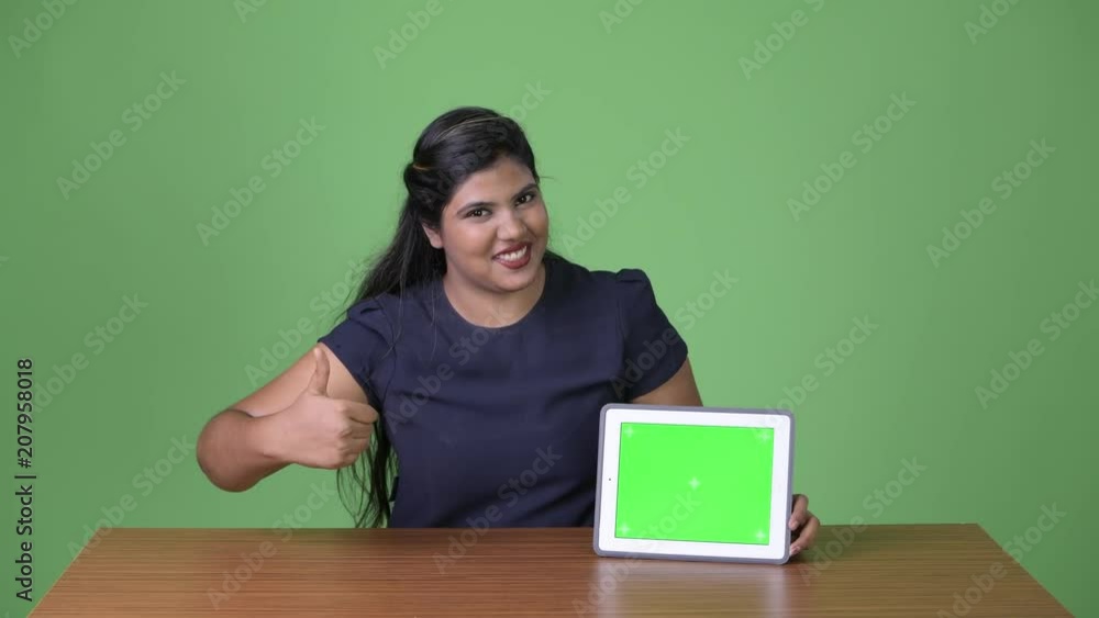 Young overweight beautiful Indian businesswoman against green background Young overweight beautiful Indian businesswoman against green background