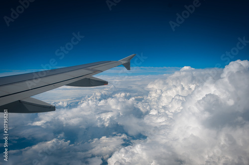 Beautiful view of the airplane wing and white loose clouds in the blue sky from the window of the plane.