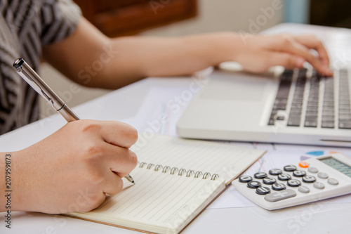 woman hand writing make note and using laptop on paper graph data with doing finance at office.