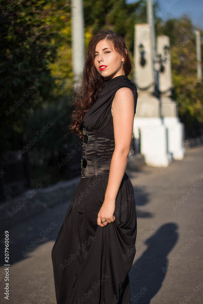 Young, beautiful girl in a black dress with a corset, on a park background and stone columns with lanterns. Young, beautiful girl in a black dress with a corset, on a park background and stone columns with lanterns.