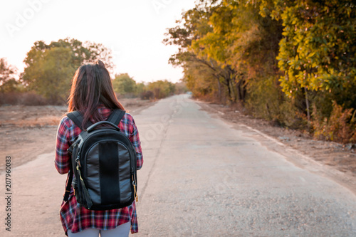Travel concept. Traveling woman with backpack walking on asphalt road countryside