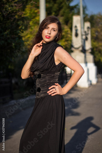 Young, beautiful girl in a black dress with a corset, on a park background and stone columns with lanterns.