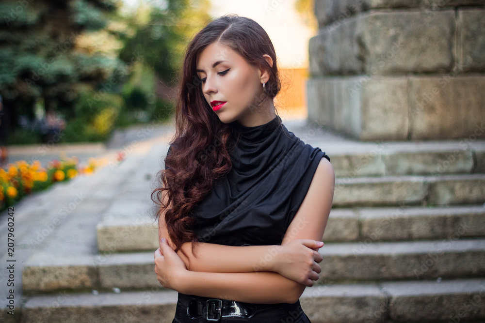 Young, beautiful girl in a black dress with a corset, in the background of a park and stone steps and flowers. Young, beautiful girl in a black dress with a corset, in the background of a park and stone steps and flowers.