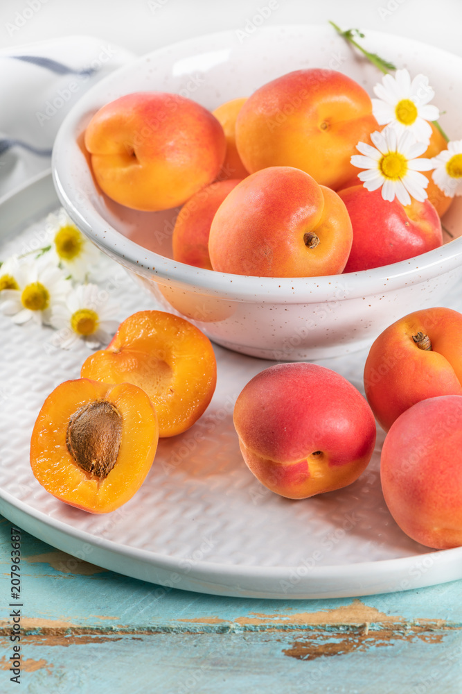 Delicious ripe apricots in a bowl on the wooden table. Close-up with apricots and daisy flowers Delicious ripe apricots in a bowl on the wooden table. Close-up with apricots and daisy flowers