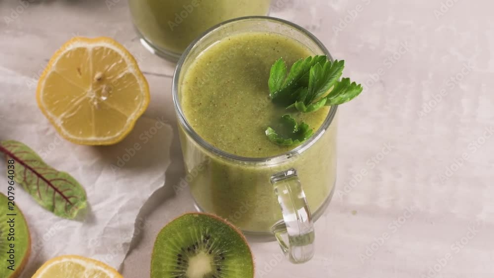 Glasses of green vegetable smoothie. Green vegetable smoothie and ingredients: Kiwi, lemon and herbs. Glasses of green vegetable smoothie. Green vegetable smoothie and ingredients: Kiwi, lemon and herbs.