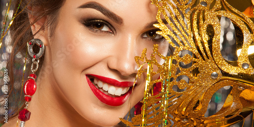 Beautiful girl with a gold mask close-up. Celebration. Bright makeup and hair, shiny background.
