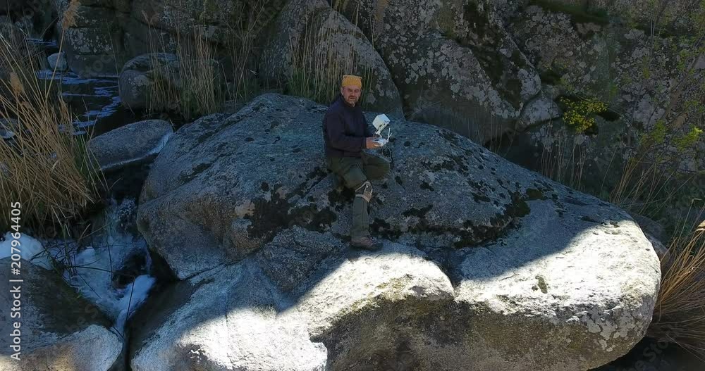 Aerial view. Mature Man operating drone with remote controller outdoors. Summer Landscape on a canyon and fast river at bottom of cliff Aerial view. Mature Man operating drone with remote controller outdoors. Summer Landscape on a canyon and fast river at bottom of cliff