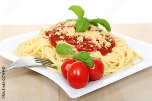Spagetti z sosem bolońskim serem, pomidorami i zielonymi listkami bazyli.