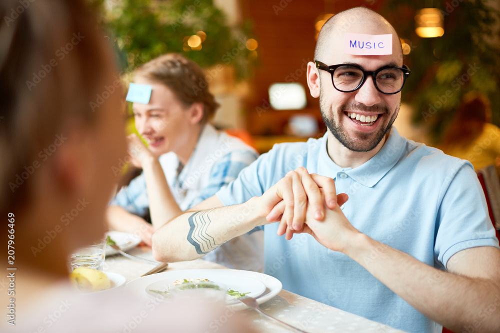 Crop view of young people playing game with scraps paper on foreheads and smiling in cafe Crop view of young people playing game with scraps paper on foreheads and smiling in cafe