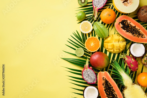 Fototapeta Egzotyczne owoce i tropikalne liście palmowe na pastelowym żółtym tle - papaja, mango, ananas, banan, karambola, smok owoc, kiwi, cytryna, pomarańcza, melon, kokos, wapno. Widok z góry.