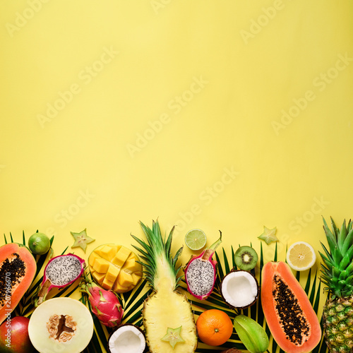 Fototapeta Naklejka Na Ścianę i Meble -  Exotic fruits and tropical palm leaves on pastel yellow background - papaya, mango, pineapple, banana, carambola, dragon fruit, kiwi, lemon, orange, melon, coconut, lime. Top view.