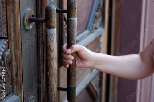 A beautiful girl tries to open a heavy antique door.