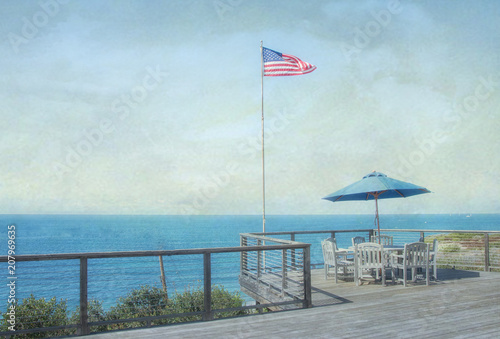 Textured photograph of a deck with table, chairs and American flag overlooking the ocean © Janice
