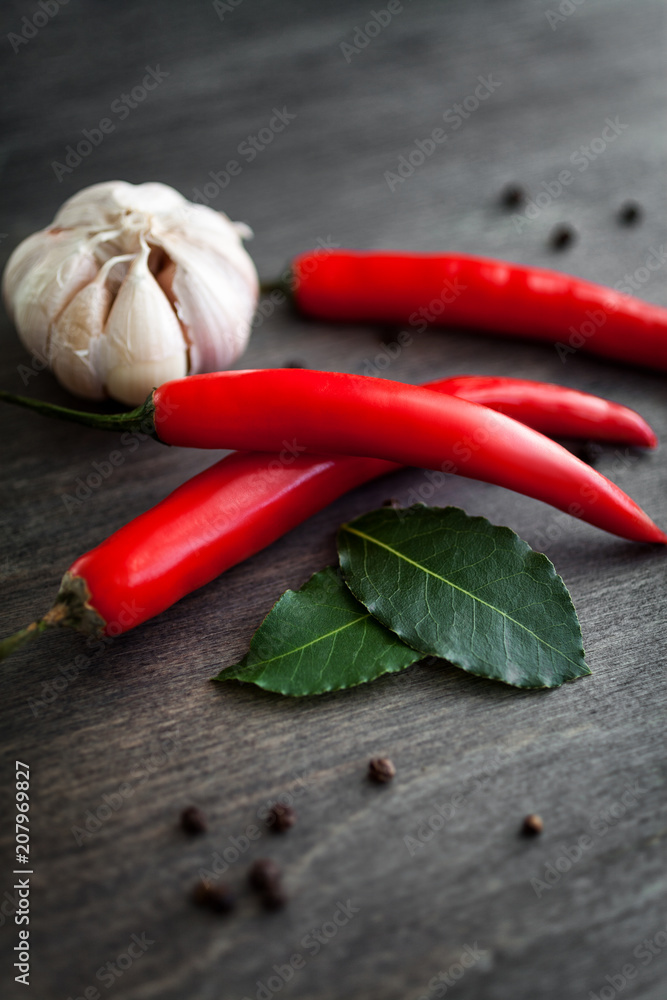 Fototapeta Czerwonego chili pieprze, czosnek, liść laurowy, rozmarynowe i różnorodne pikantność na czarnym drewnianym tle ,.