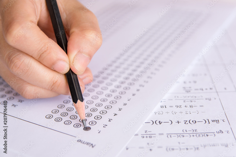 Students hand holding pencil writing selected choice on answer sheets and Mathematics question sheets. students testing doing examination. school exam Students hand holding pencil writing selected choice on answer sheets and Mathematics question sheets. students testing doing examination. school exam