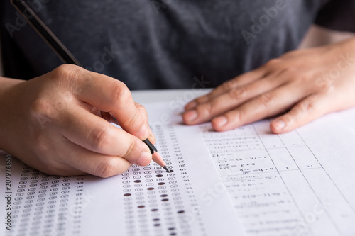 Exam. Students holding pencil writing selected choice on answer sheets and Mathematics question sheets. students testing doing examination. school exam	 photo